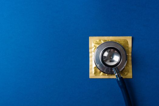 World sexual health or Aids day, Top view flat lay medical equipment, condom in pack and stethoscope, studio shot isolated on dark blue background, Safe sex and reproductive health concept