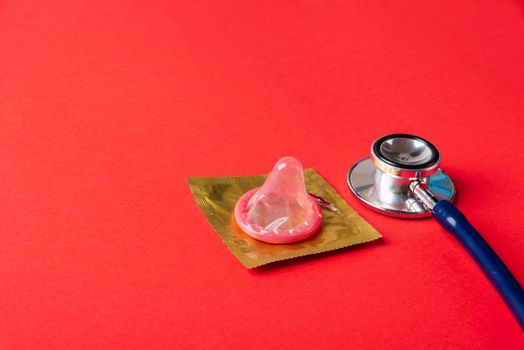 World sexual health or Aids day, Top view flat lay medical equipment, condom in pack and stethoscope, studio shot isolated on a red  background, Safe sex and reproductive health concept