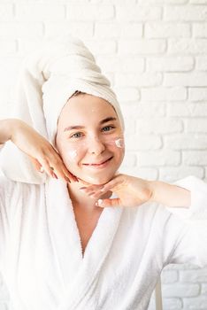 Spa and wellness. Natural cosmetics. Self care. Happy young caucasian woman in white bath towel applying face cream at home