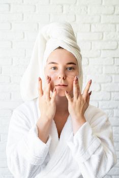 Spa and wellness. Natural cosmetics. Self care. Happy young caucasian woman in white bath towel applying face cream at home