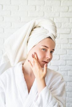 Spa and wellness. Natural cosmetics. Self care. Happy young caucasian woman in white bath towel applying face cream at home