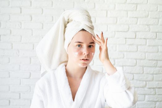 Spa and wellness. Natural cosmetics. Self care. Happy young caucasian woman in white bath towel applying face cream at home