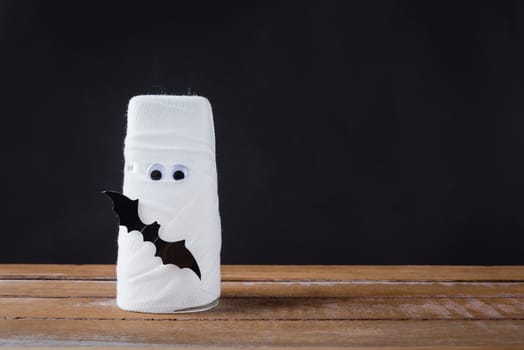 Funny Halloween day decor party concept, The mummy ghost on water glass wrapped around with bandage and have bats and spider stick it found only eyes, studio shot isolated on black background