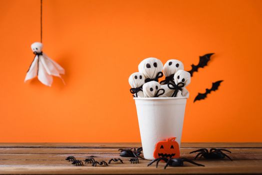 Funny Halloween day decoration party, White ghost crafts scary face head in paper cup on wood table, studio shot isolated on orange background have spider and bats, Happy holiday DIY concept