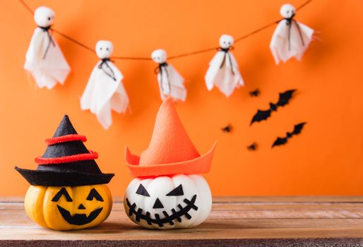Funny Halloween day decoration party, Cute pumpkin ghost spooky jack o lantern face wear hat, black spider and bats on wooden table, studio shot isolated on an orange background, Happy holiday concept