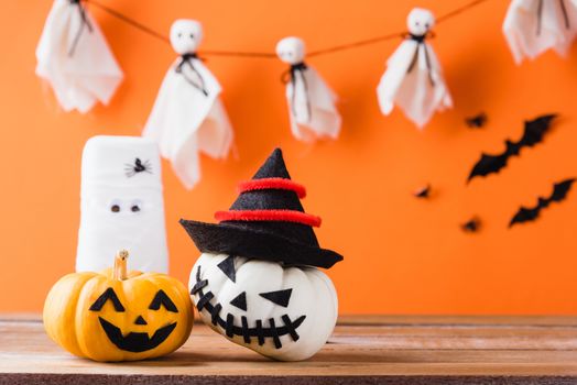 Funny Halloween day decoration party, White ghost scary face, glass of water wrapped with bandage and pumpkin on wood table, studio shot isolated on orange background