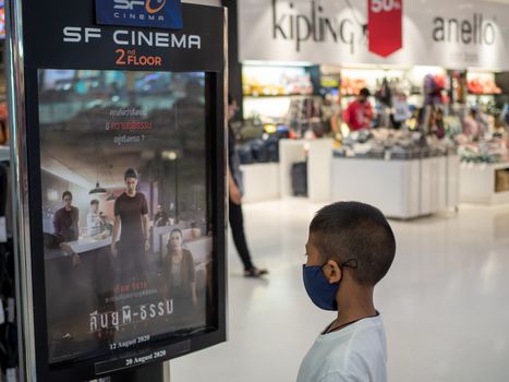 Prachinburi, Thailand 22/8/2020 Editorial illustrations Of a boy wearing a protective mask Standing and watching the billboard of the cinema In a mall in Thailand While the global coronavirus outbreak continues.