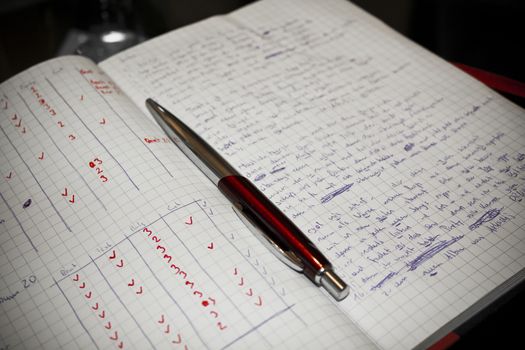 Red ballpoint pen and writing pad with written lyrics and rhyming verses.