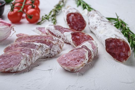 Dry cured fuet salami sausage slices with herbs on white textured background.