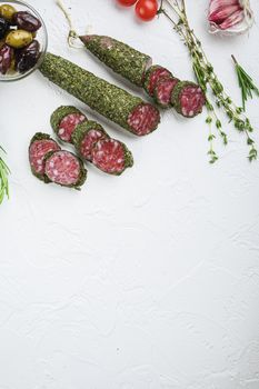Traditianal fuet sausage in herbs with ingredients on white textured background, topview with space for text.