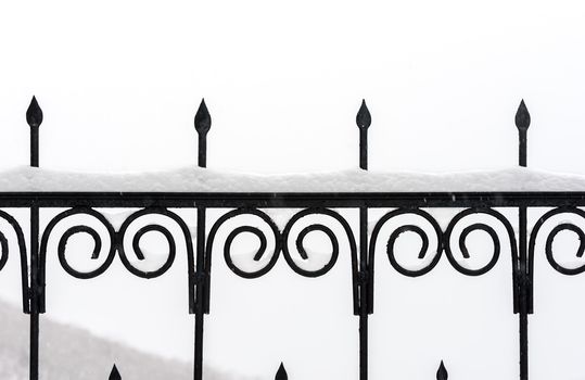 Black metal fence closeup. Snow on fence