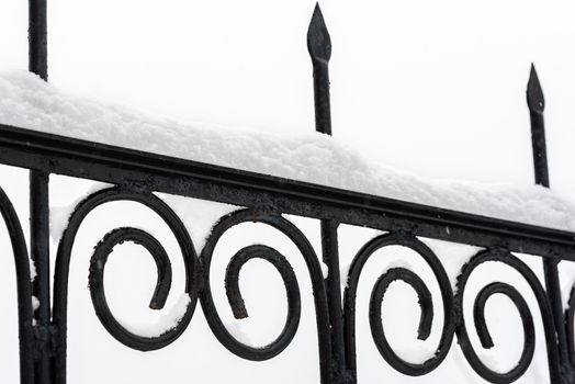 Black metal fence closeup. Snow on fence