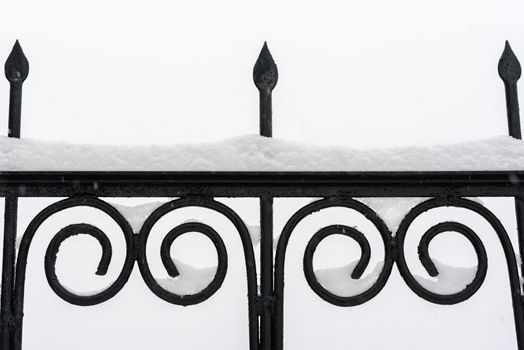 Black metal fence closeup. Snow on fence