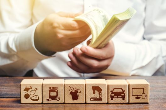 A man is counting money on the background of blocks with goods attributes. Import and export of goods and products. Retail and sales. Trade surplus, high purchasing power. Economic recovery.