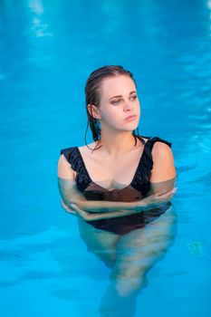 Young beautiful girl in black swimsuit in the pool posing