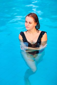 Young beautiful girl in black swimsuit in the pool posing