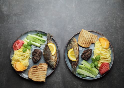 Fried fish, meat steak and vegetables on a plate. Concrete gray countertop. High quality photo