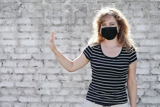 Portrait of a Girl in a protective mask, free space for text. Social distancing. White brick wall in the background. Shows stop by hand