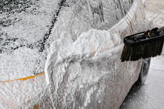 Detail on car side mirror completely covered with soap foam, more spraying from brush, when washed in carwash.