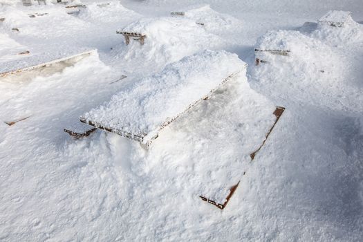 Wooden benches and desk on restaurant terrace barely visible under heavy load of snow. Concept illustrating extreme snowfall.