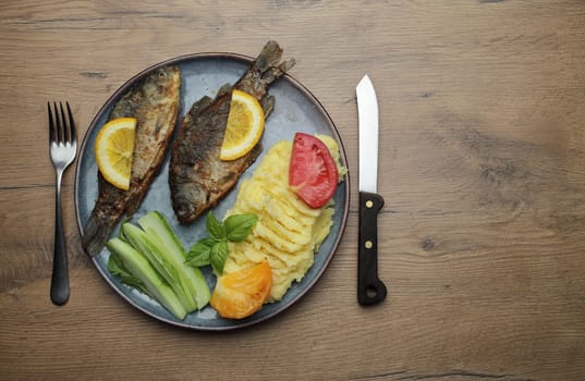 Fried fish and vegetables on a plate. On a wooden table. High quality photo