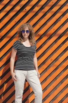 Woman portrait in sunglasses, free space for text. Orange wooden wall in the background