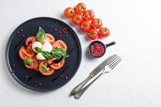 Tomato, basil, mozzarella Caprese salad ib bowl with fork with balsamic vinegar and olive oil. white background over head top view space for text horizontal photo.