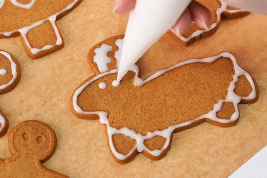 Young woman is decorating Christmas Gingerbread House cookies biscuit at home with frosting topping in icing bag, close up, lifestyle.