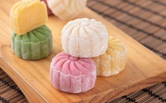 Colorful snow skin moon cake, sweet snowy mooncake, traditional savory dessert for Mid-Autumn Festival on bright wooden background, close up, lifestyle.