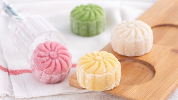 Colorful snow skin moon cake, sweet snowy mooncake, traditional savory dessert for Mid-Autumn Festival on bright wooden background, close up, lifestyle.