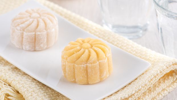 Colorful snow skin moon cake, sweet snowy mooncake, traditional savory dessert for Mid-Autumn Festival on bright wooden background, close up, lifestyle.