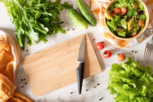 Healthy food concept. Top view of making vegetable salad with cutting board, bowl of salad and fresh organic vegetables