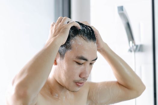 Closeup young man washing hair with with shampoo in the bathroom, vintage tone, selective focus