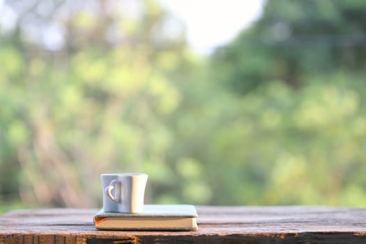 White cup with notebook on wooden table with nature view