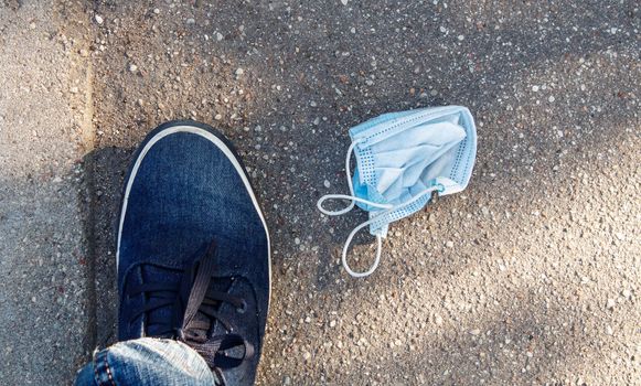 protective medical mask on the sidewalk with male foot closeup on summer day