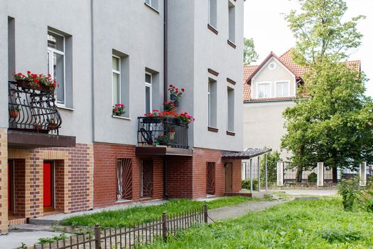 new house with plastic windows and doors in a residential area with red flowers on balconies on summer day