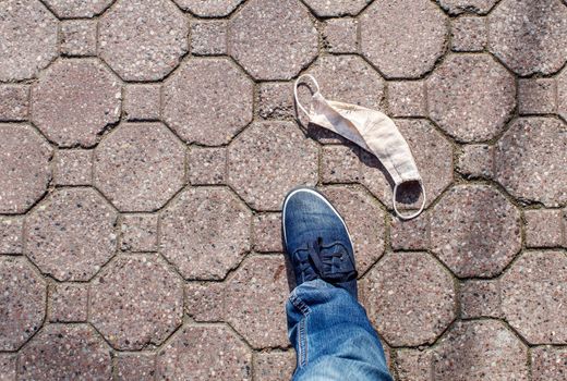 protective medical mask on the sidewalk with male foot on summer day