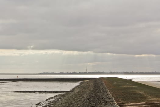 Water, clouds, dike and shells on the north German coast of Butjardingen in Lower Saxony, Germany.