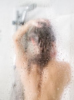 Beautiful young woman washing head in a shower. Glass with drops