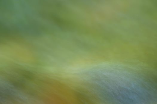 Long exposure image of a woodland stream flowing over stones. Forest colors are reflected in teh moving water. Natural light, with copy space.