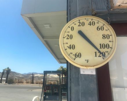 round outdoor gas station thermometer reads 118 degrees F under a blue sky with copy space.