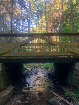 Full frame image in natural light shows a very beautiful wooden footbridge over a foeest stream with colorful woodland foliage background.