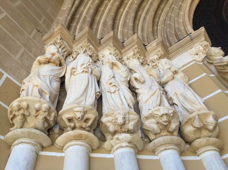 Fourteenth century statues of five apostles rise on columns at the entrance to the cathedral in Évora, Portugal. Low-angle image shot in natural light shows lovely color and detalil of figural base.