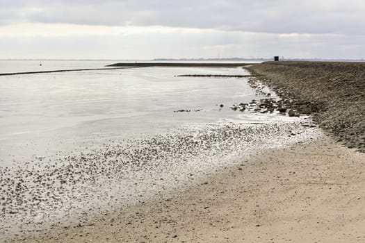 Water, clouds, dike and shells on the north German coast of Butjardingen in Lower Saxony, Germany.