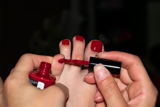 a girl's hand paints her toenails with red nail Polish in the evening at home