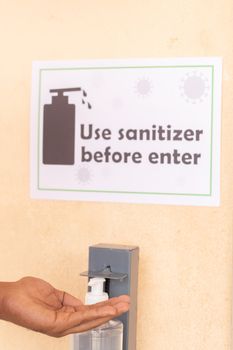 Close up of hands using hand sanitizer below the use sanitizer before enter signage board on wall as safety measure due to coronavirus or covid-19 pandemic.