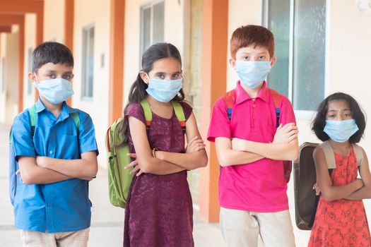 Children in medical mask with school backpack standing with arms crossed by looking to the camera- Concept of back to school and reopen