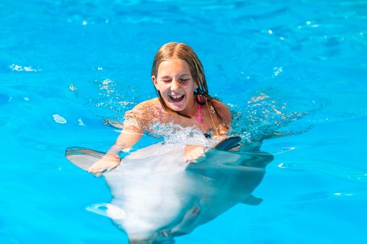 Happy little girl swimming with dolphins in Dolphinarium. Swimming, bathing and communication with dolphins.