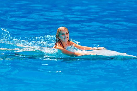 Happy little girl swimming with dolphins in Dolphinarium. Swimming, bathing and communication with dolphins.