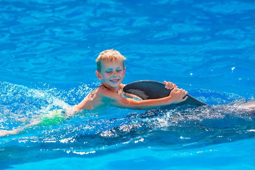 Happy little boy swimming with dolphins in Dolphinarium. Swimming, bathing and communication with dolphins.